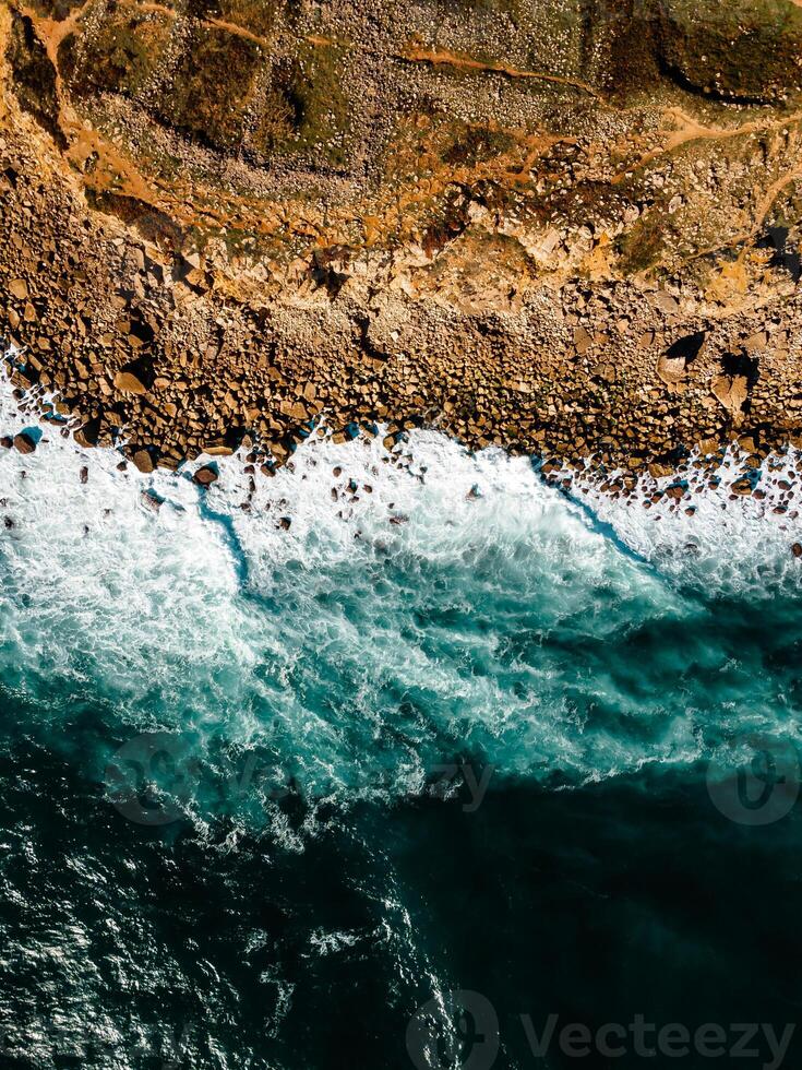 Aerial view of rocky beach with waves and clear ocean water. Drone top view photo