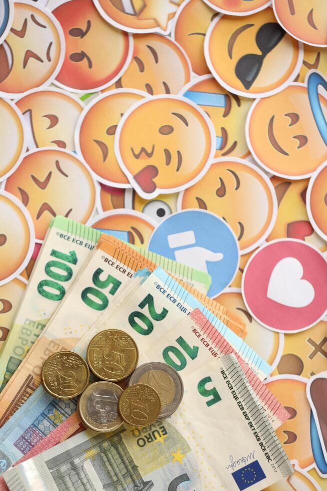 KYIV, UKRAINE - APRIL 20, 2024 European euro money and large set of stickers with Emoji yellow faces. The concept of smm, smo paid service for boost in social media photo