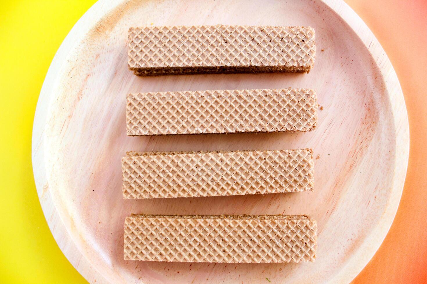 Chocolate waffles on wooden plate isolated on orange and yellow background. Crispy snack dessert. Food Photography Concept photo