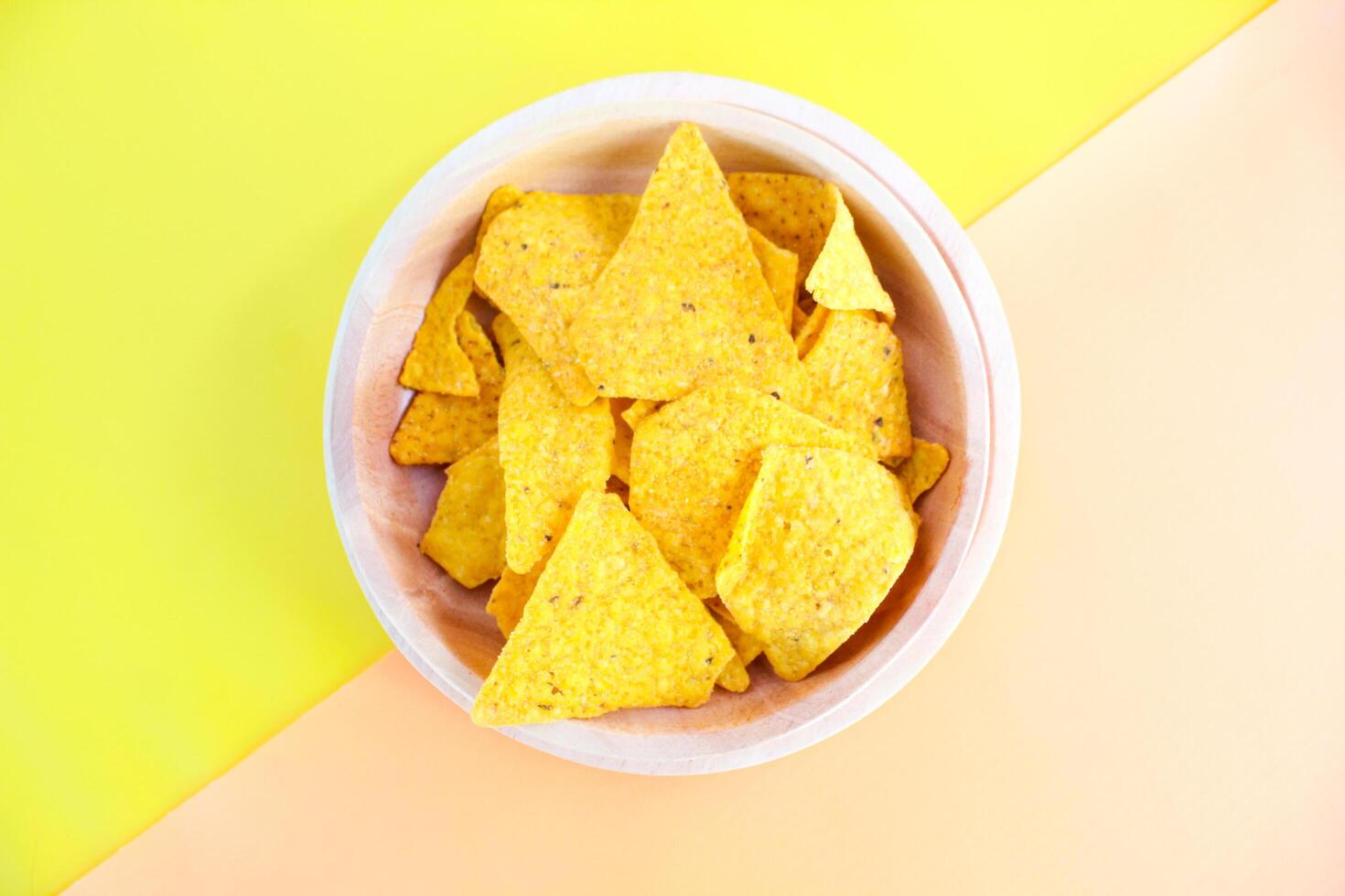 Corn chips on wooden plate isolated on orange and yellow background. Crispy snack dessert. Food Photography Concept photo