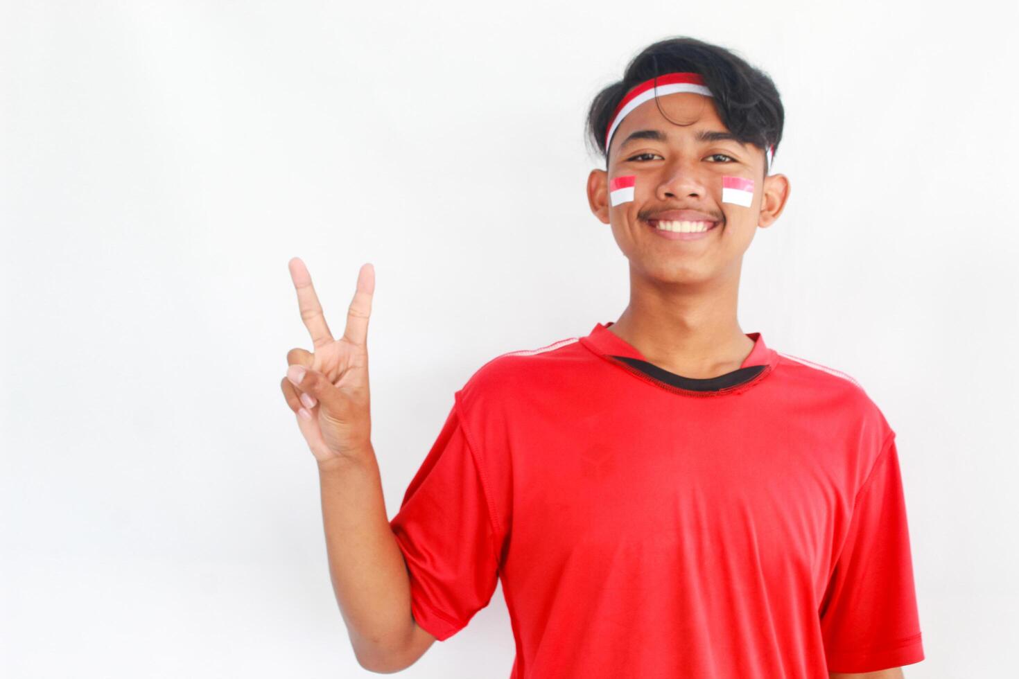 A confident young Asian man makes a number sign on an isolated white background. wearing a red shirt. Indonesian Independence day photo