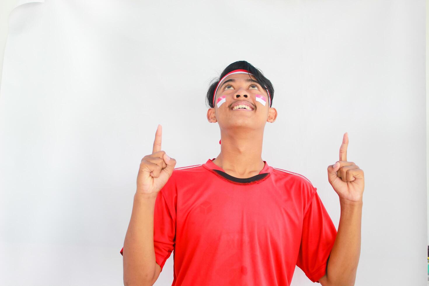 A confident young Asian man makes a number sign on an isolated white background. wearing a red shirt. Indonesian Independence day photo