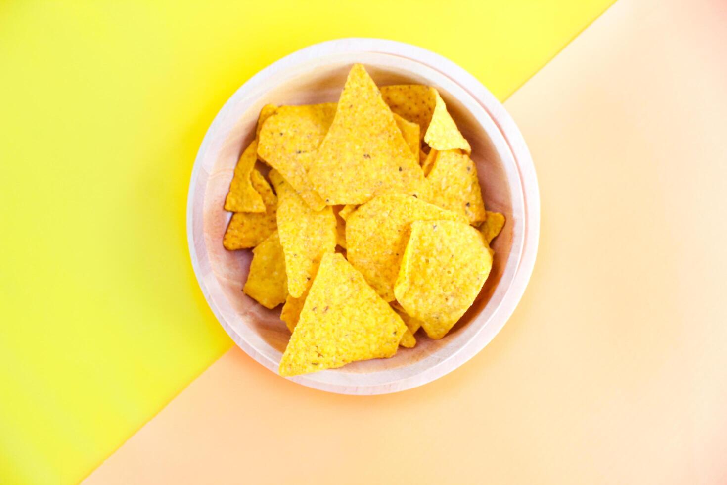 Corn chips on wooden plate isolated on orange and yellow background. Crispy snack dessert. Food Photography Concept photo
