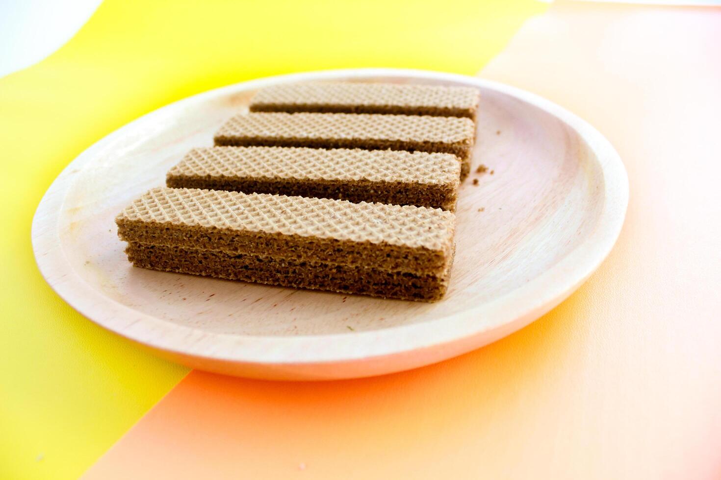 Chocolate waffles on wooden plate isolated on orange and yellow background. Crispy snack dessert. Food Photography Concept photo
