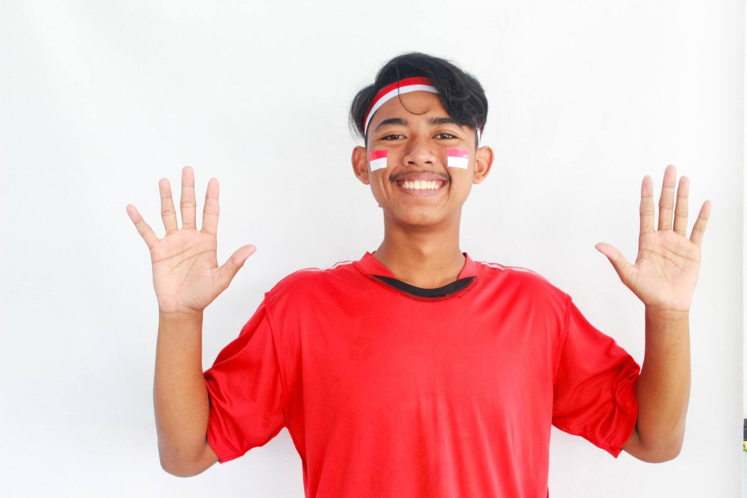 A confident young Asian man makes a number sign on an isolated white background. wearing a red shirt. Indonesian Independence day photo