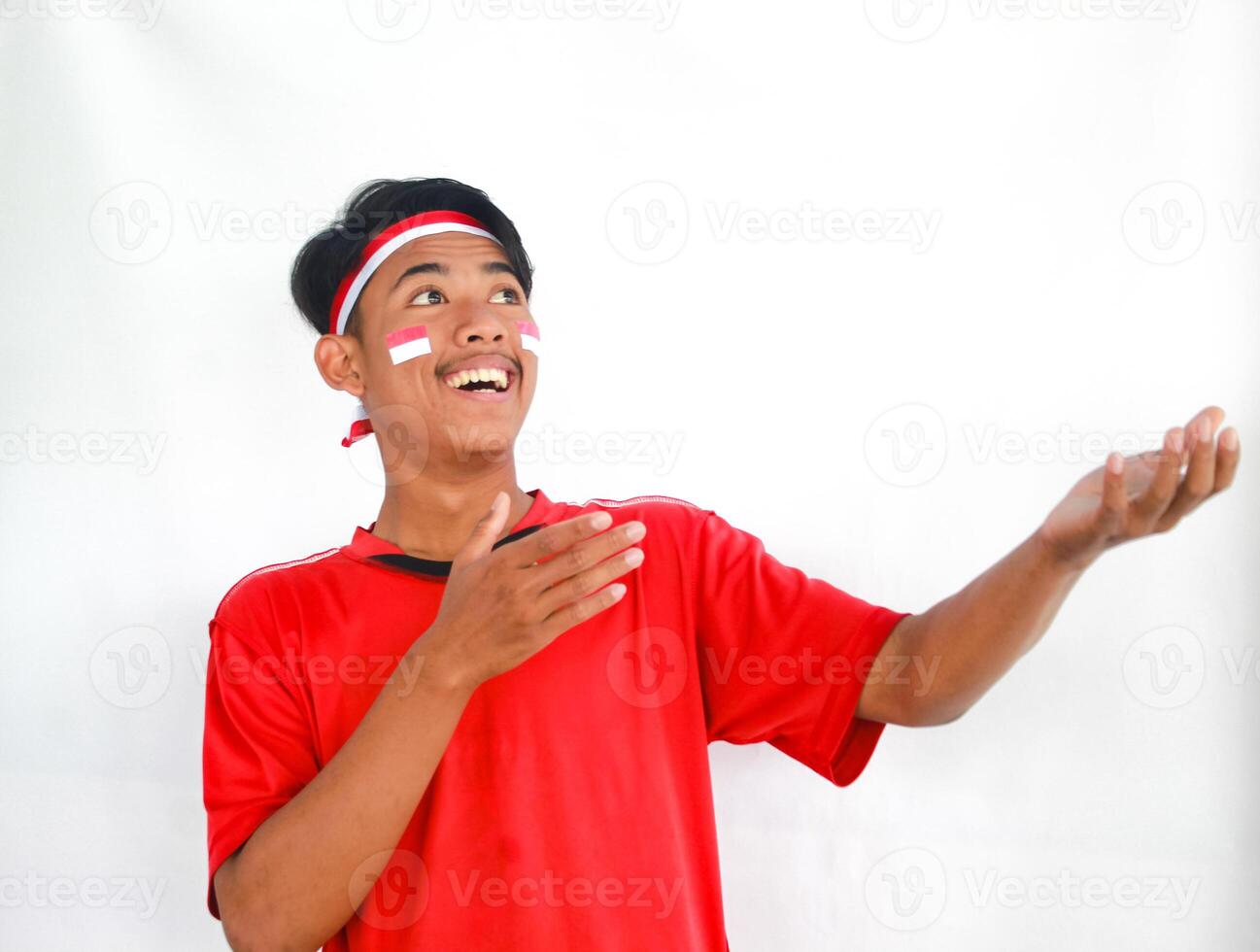 handsome young man in a red shirt and headband pointing to the copy space beside him, isolated white background, celebrating indonesia's independence day. Indonesia Independence Day concept. photo