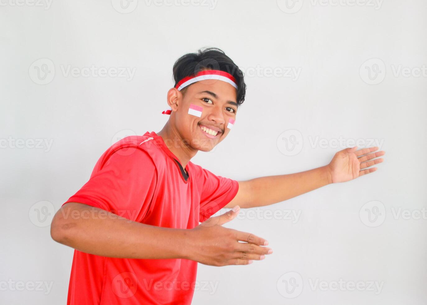 handsome young man in a red shirt and headband pointing to the copy space beside him, isolated white background, celebrating indonesia's independence day. Indonesia Independence Day concept. photo
