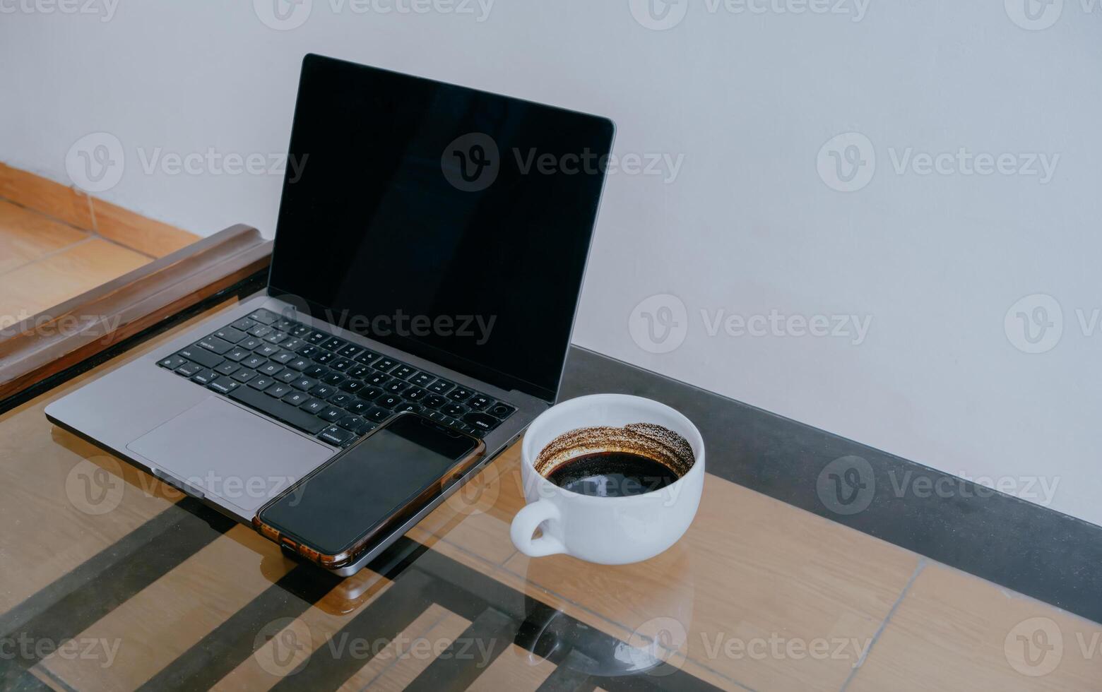 Laptop, cell phone and cup of black coffee on glass table with copy space. photo
