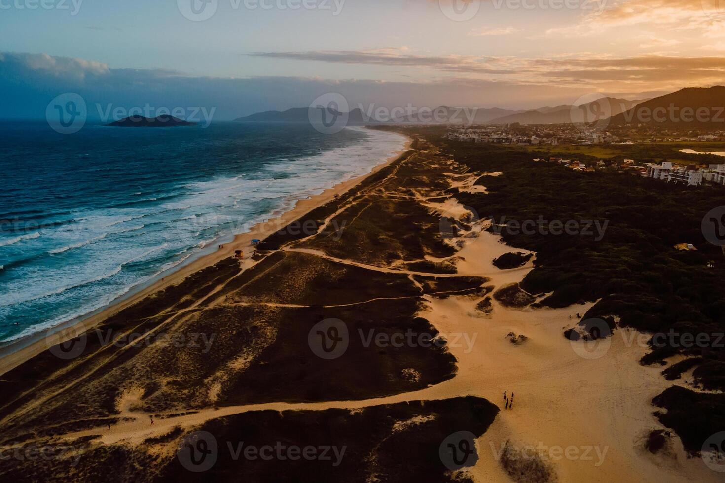 Beach with dunes, ocean and town with sunset lights in Florianopolis photo