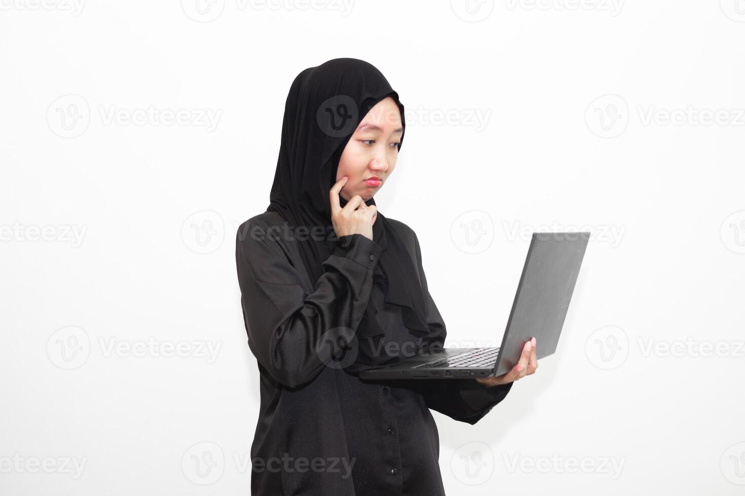 A female office worker wearing a hijab is looking at her work in front of a laptop computer while thinking. isolated in white background photo