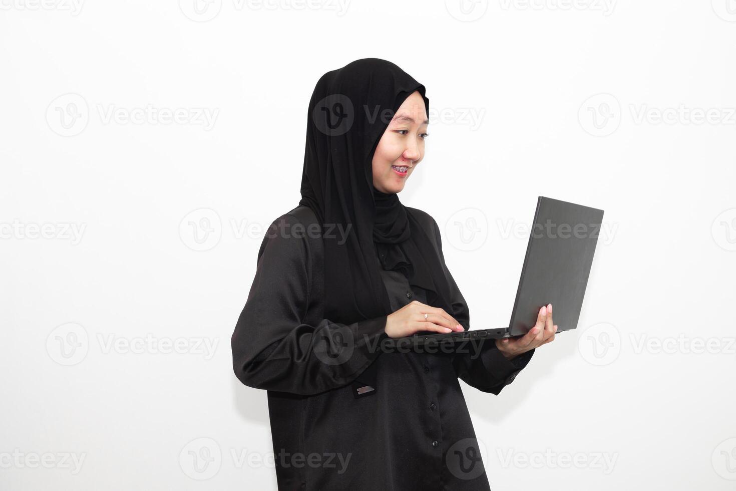 A female office worker wearing a hijab is looking at her work in front of a laptop computer with a smile and a happy face. photo