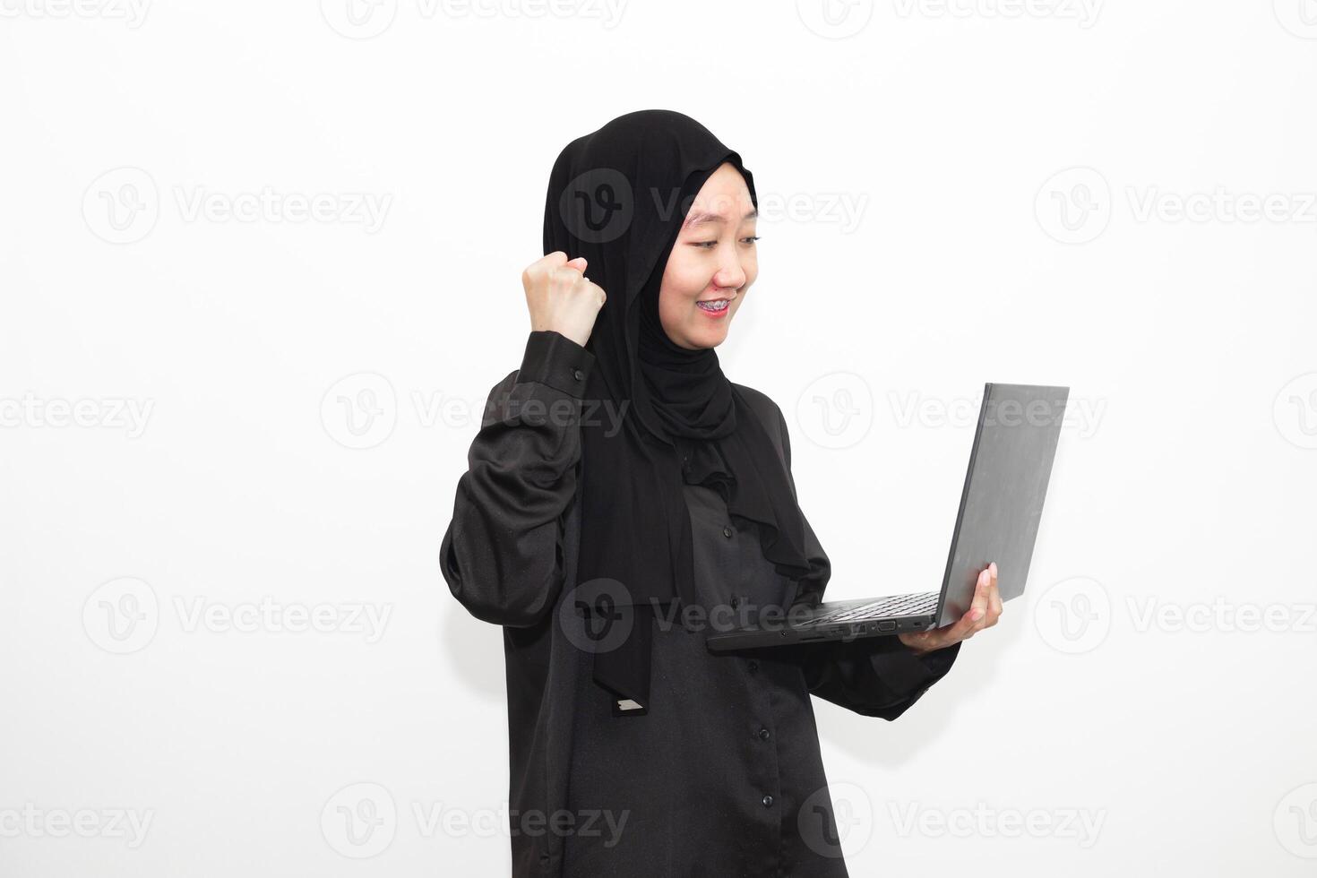 A female office worker wearing a hijab is looking at her work in front of a laptop computer with a smile and a happy face. photo