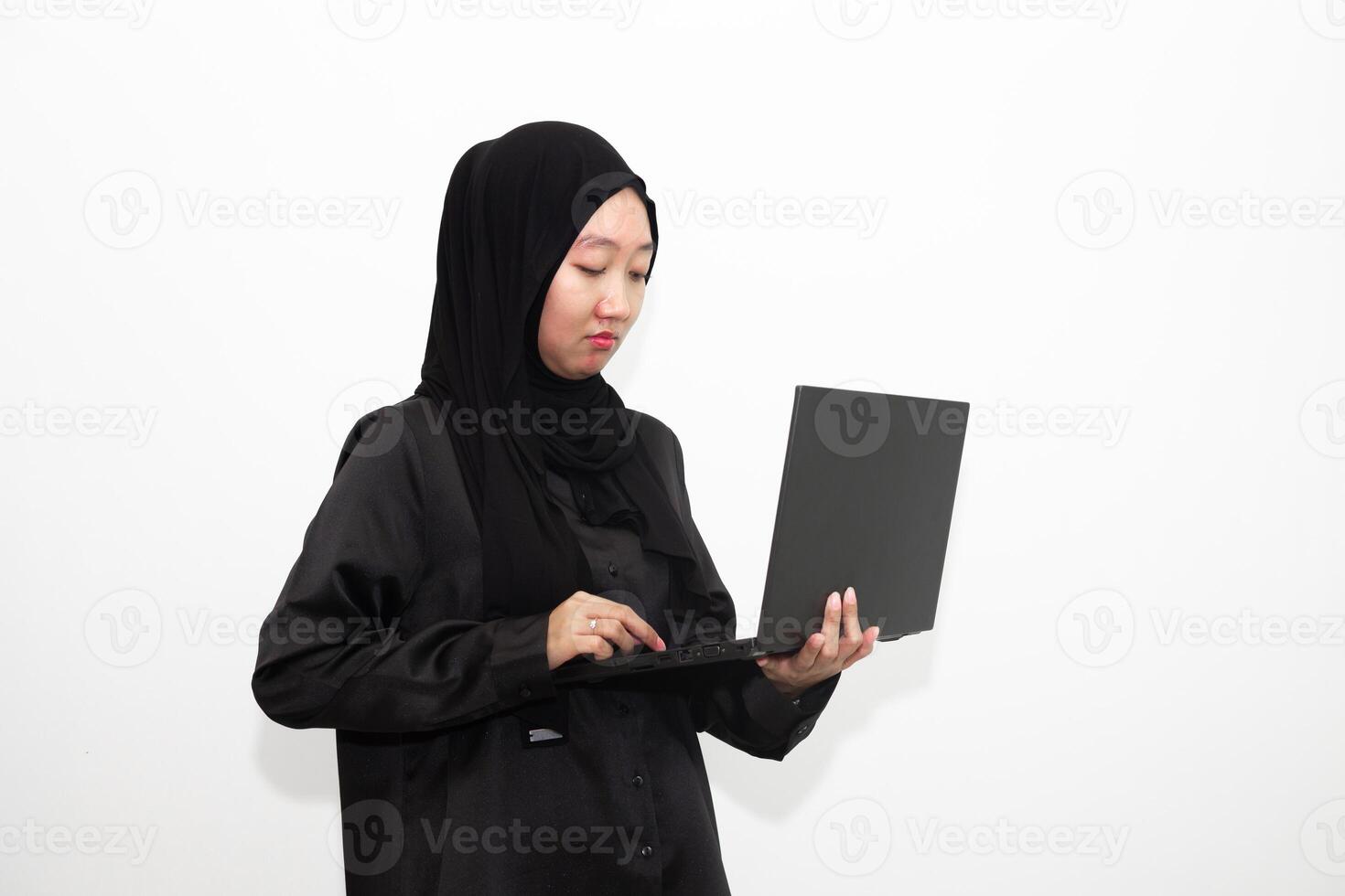 A female office worker wearing a hijab is looking at her work in front of a laptop computer while thinking. isolated in white background photo