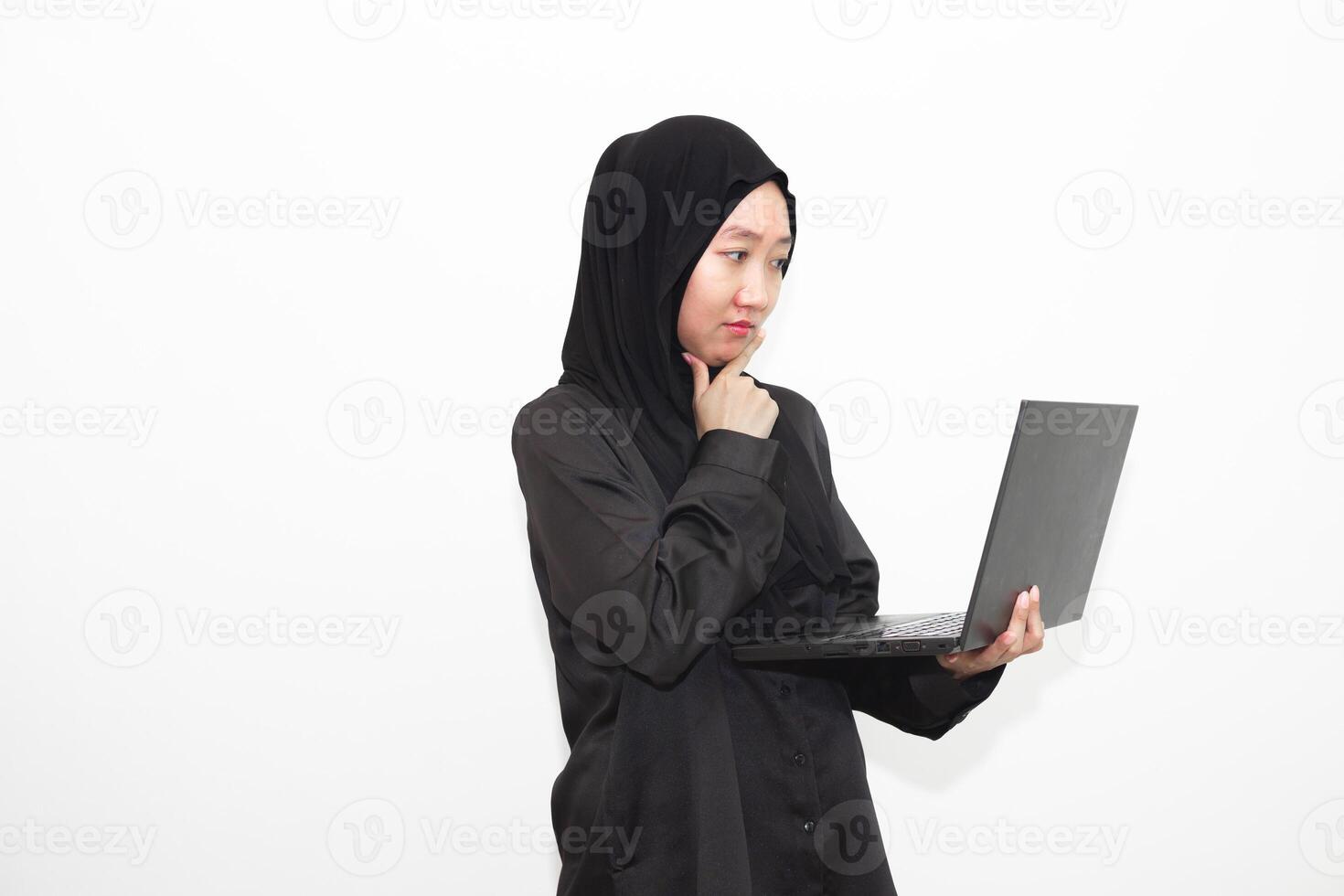 A female office worker wearing a hijab is looking at her work in front of a laptop computer while thinking. isolated in white background photo