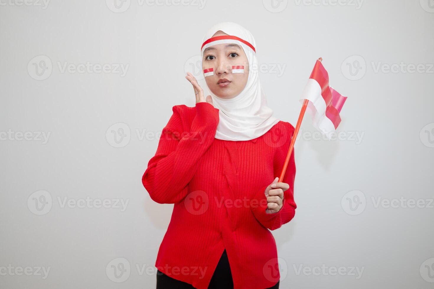 Woman in white hijab wearing red sweater. celebrating Indonesia's independence day. holding a flag with a happy face. looking at the camera. isolation on white background. photo
