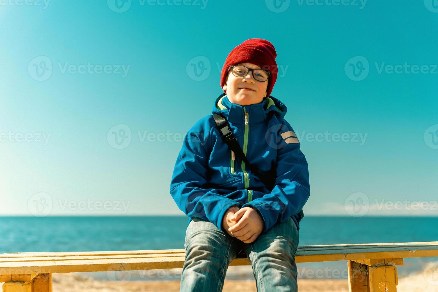 A happy boy is sitting on a bench on a sunny spring beach, walking with his family, vacations, communicating with nature photo
