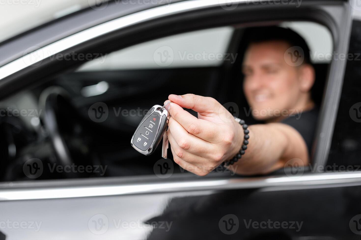 Handsome happy man driver sits in the car and holds the keys in his hand. Car rental and purchase photo