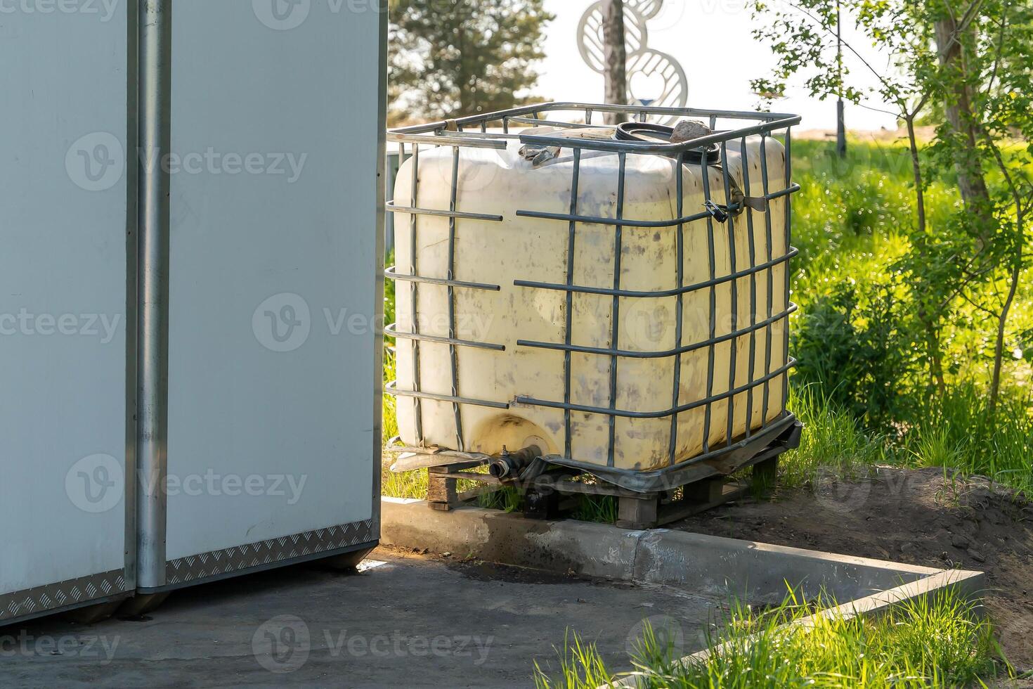 A large white plastic water tank sits on a pallet near a building photo