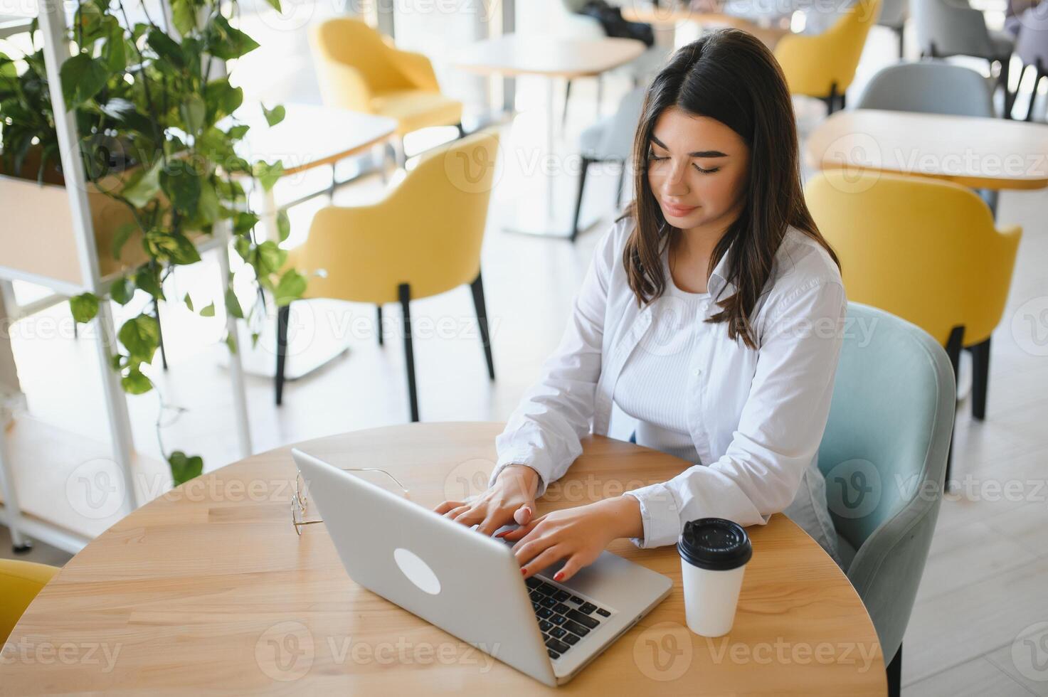 Young charming female freelancer using laptop computer for distance job while sitting in modern coffee shop interior, beautiful Caucasian woman working on net-book during morning breakfast in cafe bar photo