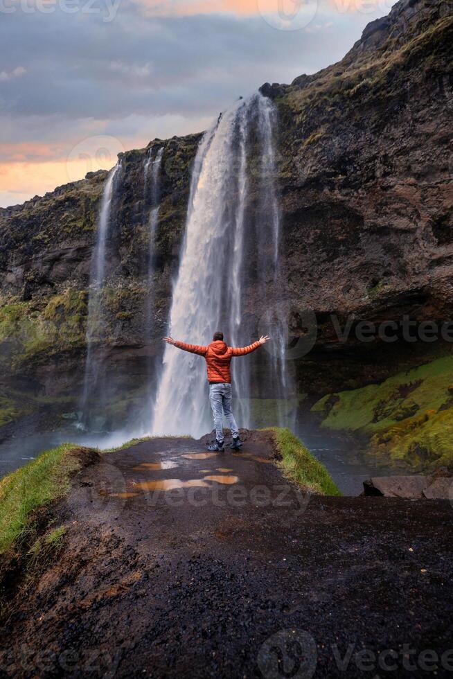 Tourist near the Majestic Seljalandsfoss Waterfall at Sunset, One of Icelands Most Iconic and Popular Tourist Attractions photo