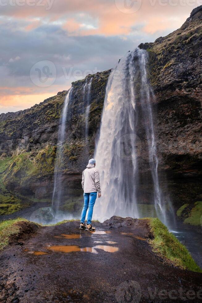 Tourist near the Majestic Seljalandsfoss Waterfall at Sunset, One of Icelands Most Iconic and Popular Tourist Attractions photo