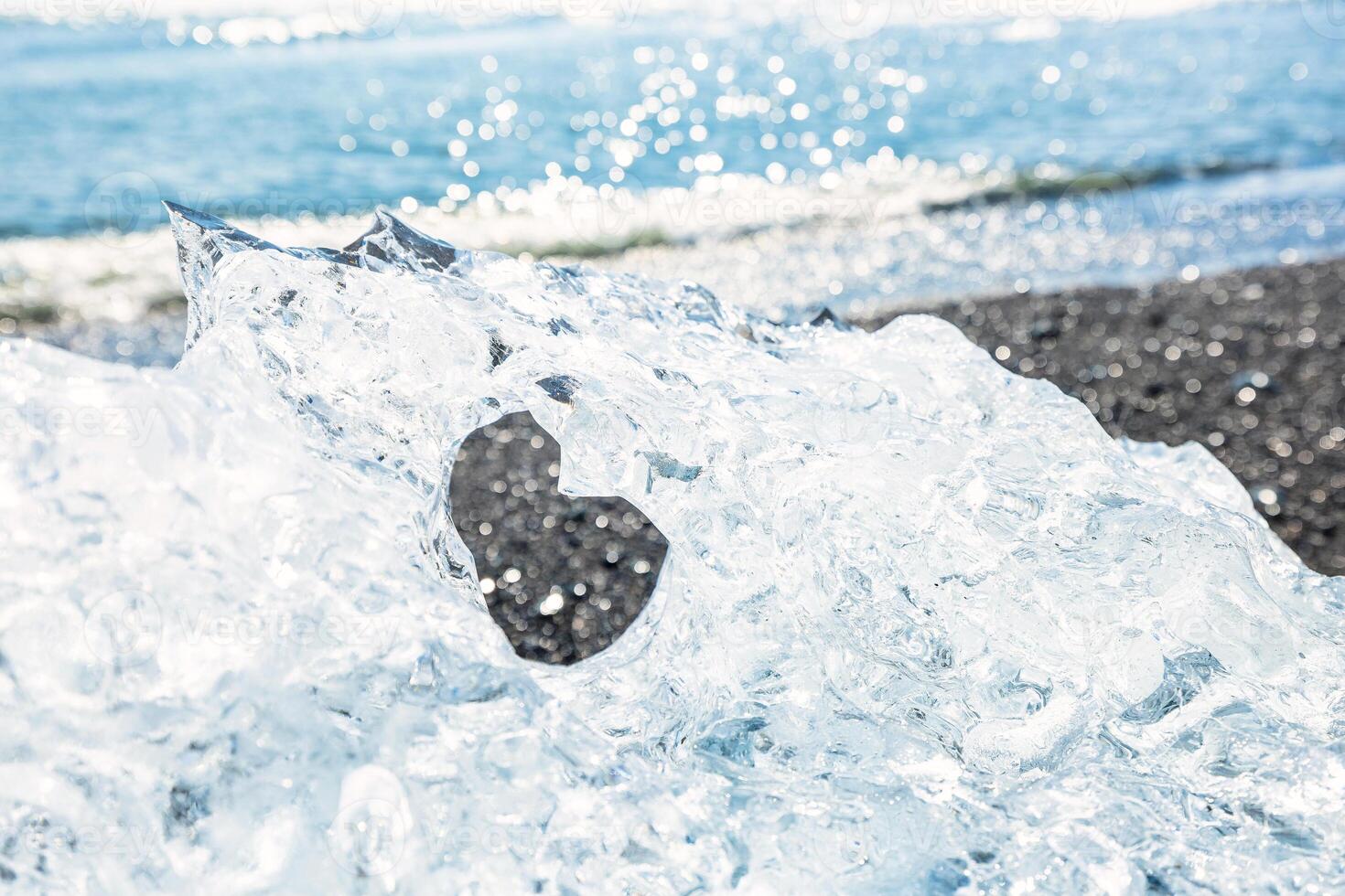 Close-up of a sparkling ice chunk on Diamond Beach in Iceland, highlighting the heart-shaped hole with the ocean in the background photo