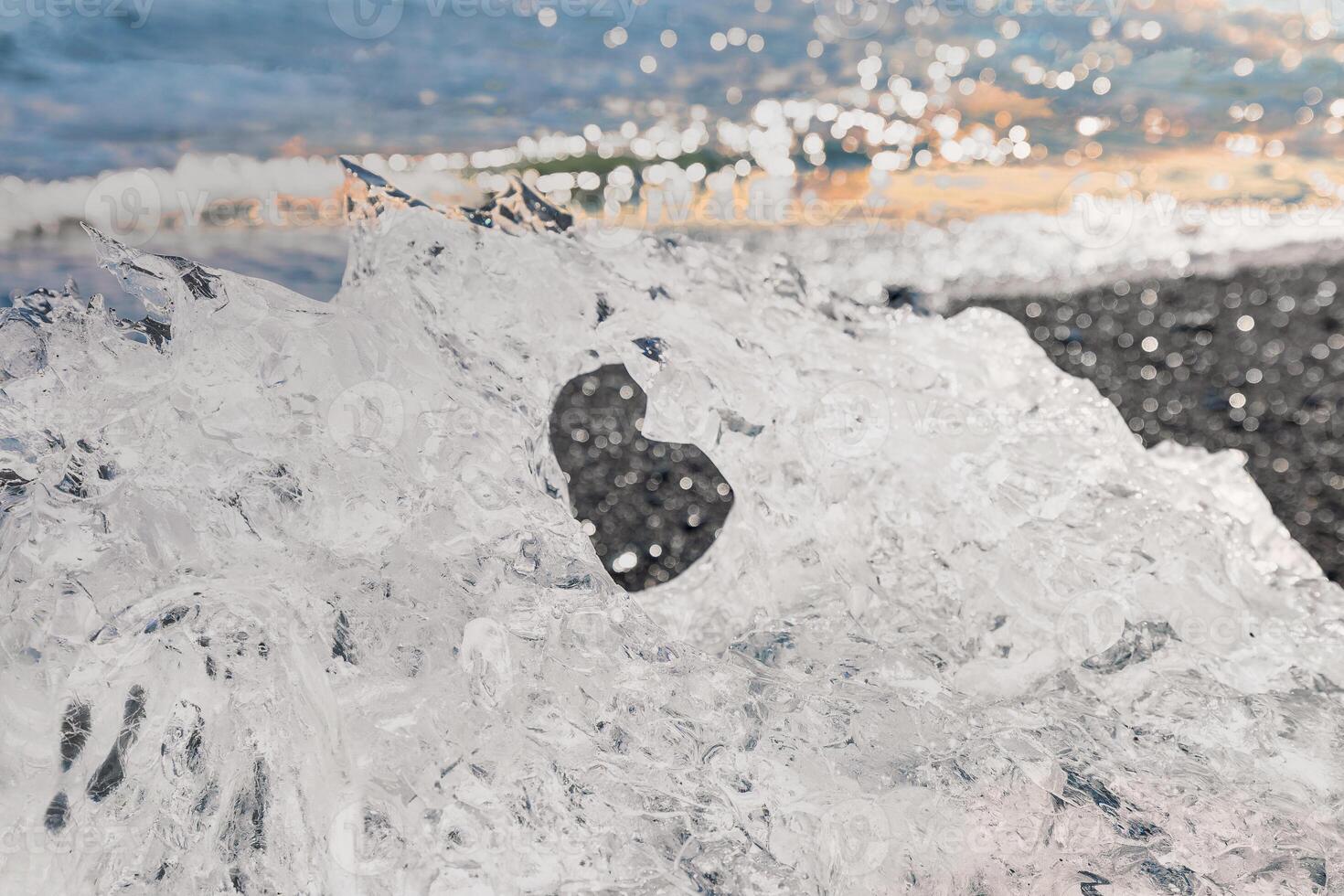Close-up of a sparkling ice chunk on Diamond Beach in Iceland, highlighting the heart-shaped hole with the ocean in the background photo