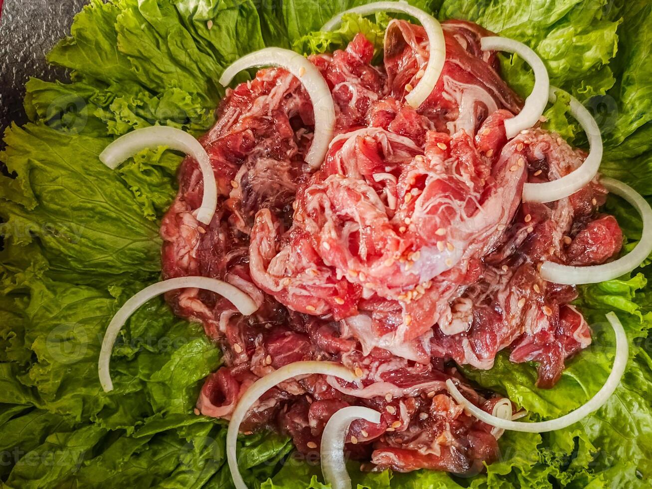 raw meat that has been prepared to be grilled Korean style with onion garnish photo
