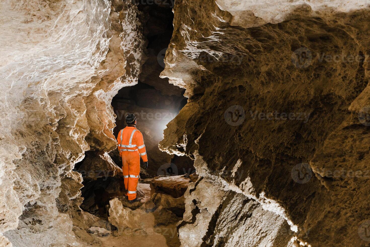 Man walking and exploring dark cave with light headlamp underground. Mysterious deep dark, explorer discovering mystery moody tunnel looking on rock wall inside. photo