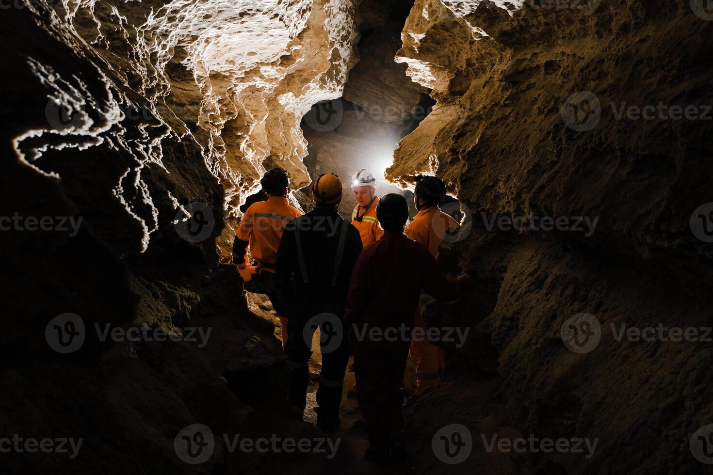 Five men, strong physique, explore the cave. Men dressed in special clothes to pass through the cave and stopped, looking at the map photo