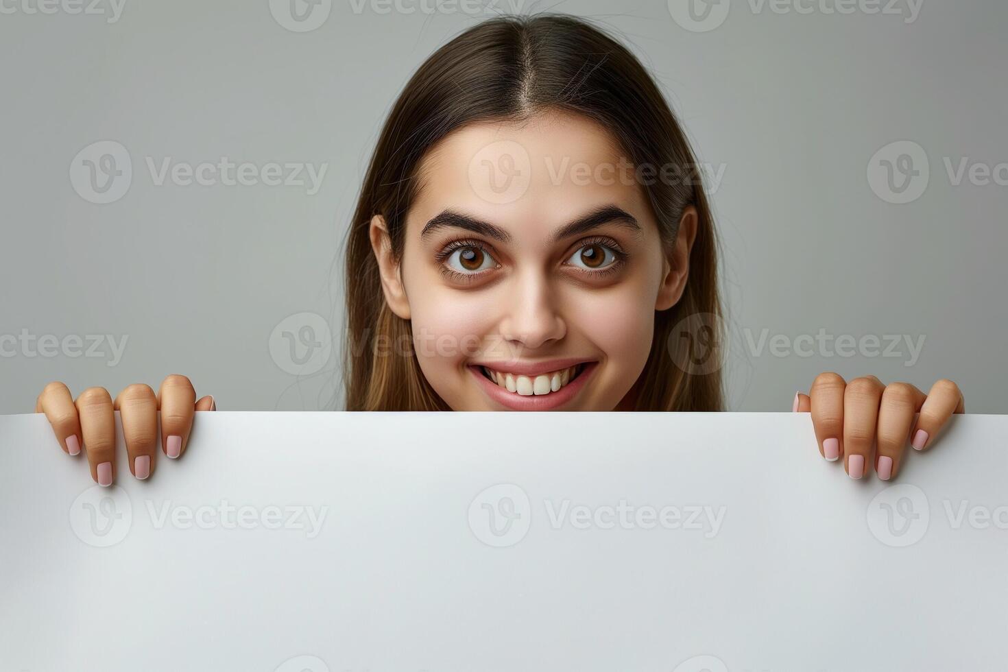 Woman Holding Blank White Board for Copy Space Smiling Playful Expression, Studio Shoot, Young Happy Girl with Hands Peeking Over Board, Close-up Portrait, Advertising Concept, Neutral Background photo