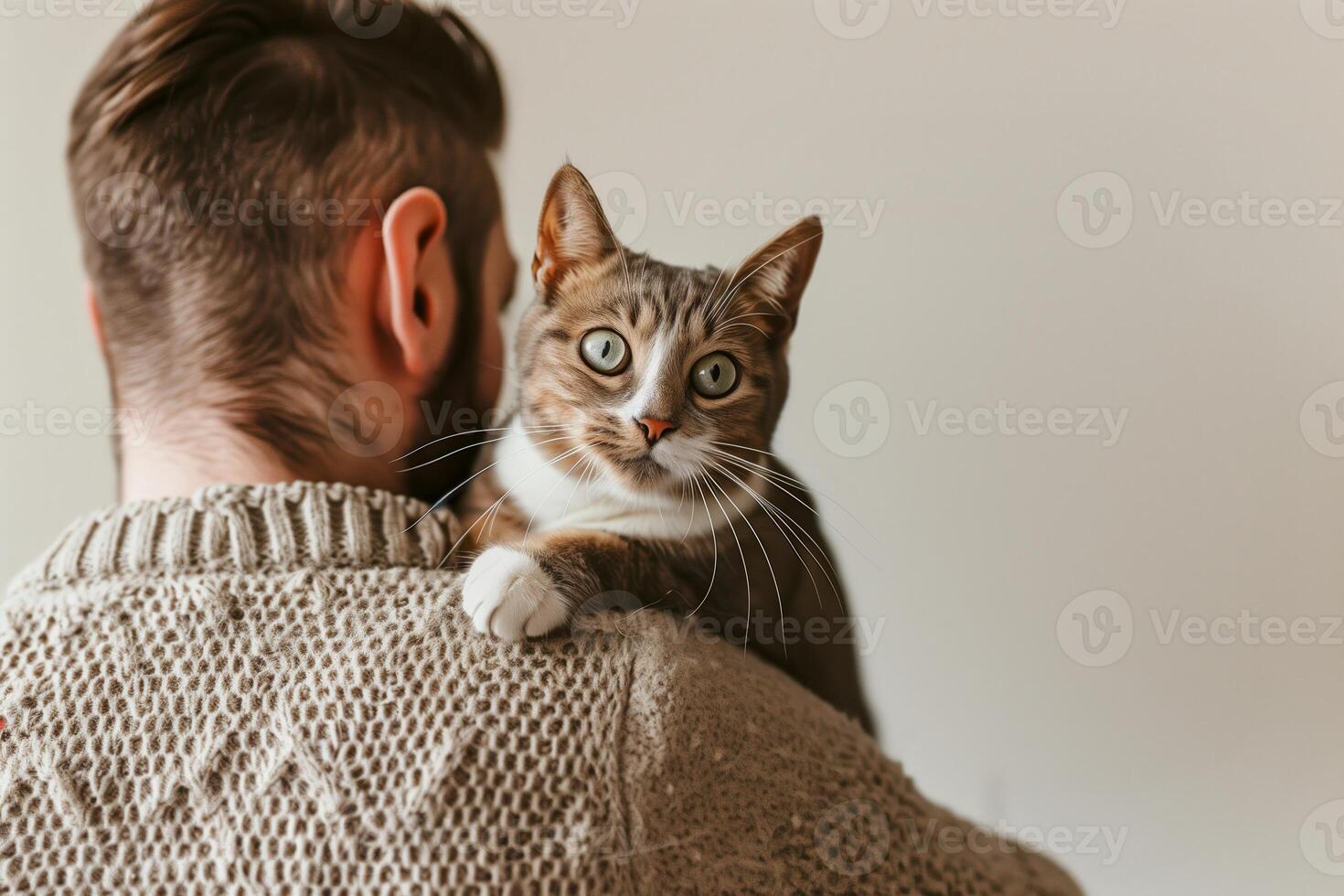 Cat Day concept. Warm Embrace With Cat, Brown Tabby Cat On Man's Shoulder, Cozy Knit Sweater, Soft Light, Home Interior, Relaxed Atmosphere, Candid Moment, Comfortable and Quiet, Feline Bonding. photo