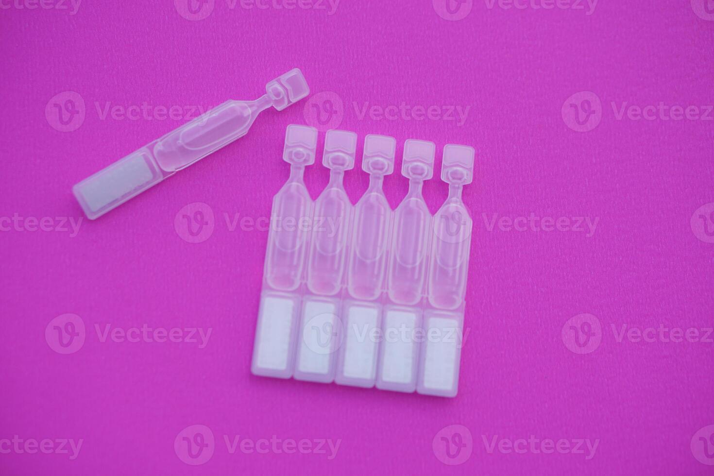 Single use artificial tear lubricant eye drops containers, tubes, isolated on pink background. Concept, medical products for dry eyes or eyes disease treatment. photo