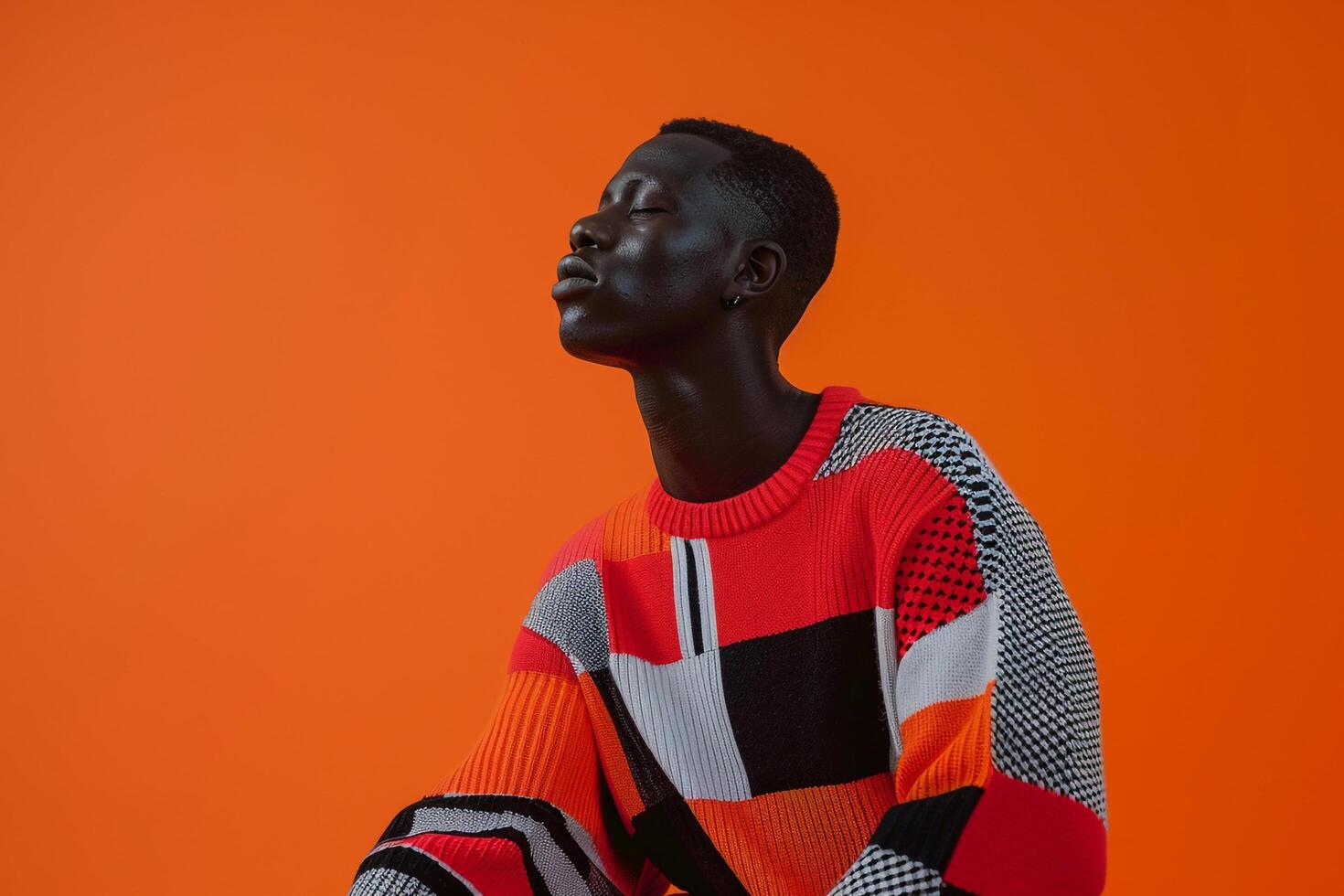 Trendy male model in a stateMalet sweater with graphic print and a bright orange backdrop highlighting a fashionable portrait and a vibrant lifestyle photo