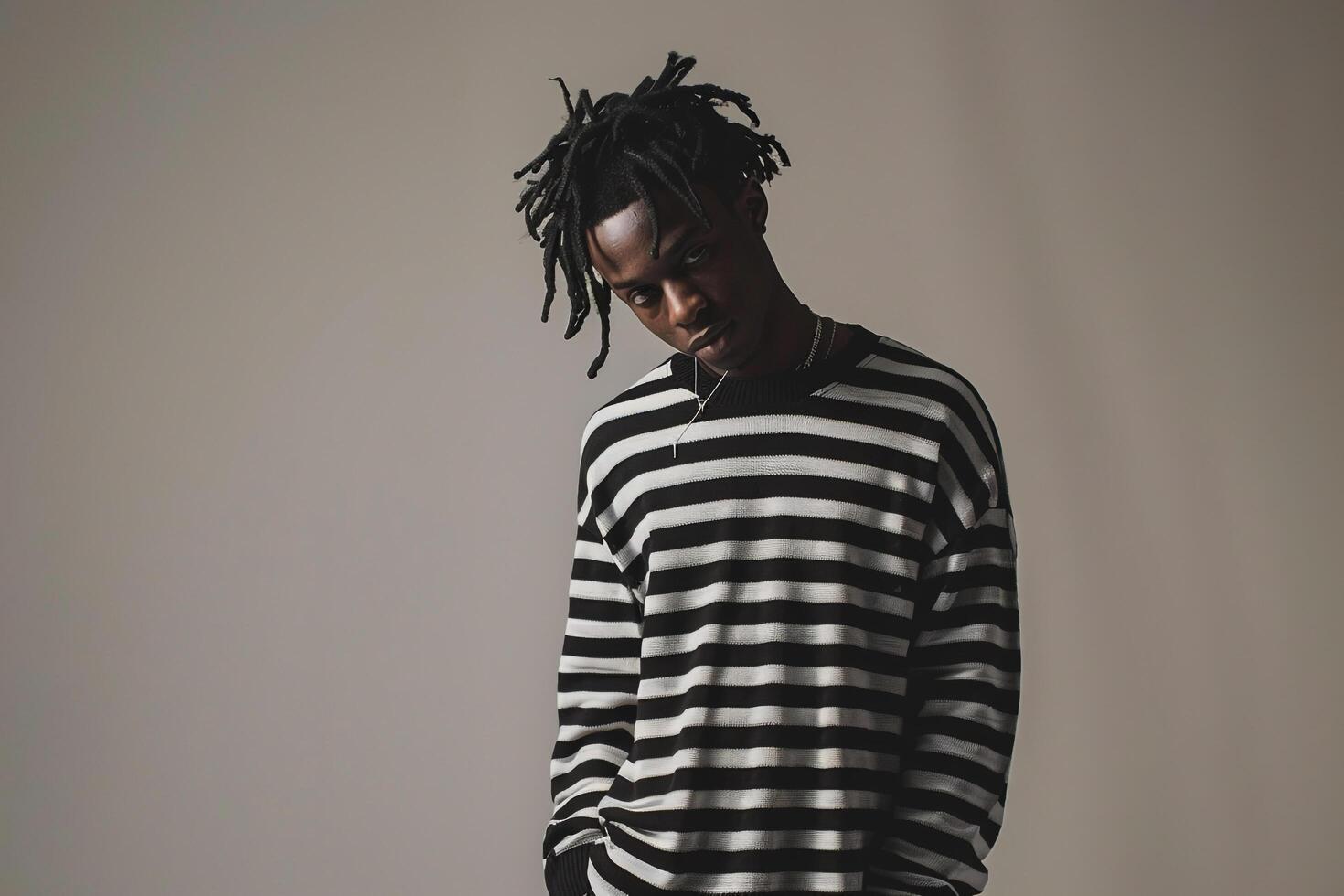 Fashionable male fashion model in black and white striped pulloverposed in male dress withlight sage Males background emphasizingfashion and lifestyle photo