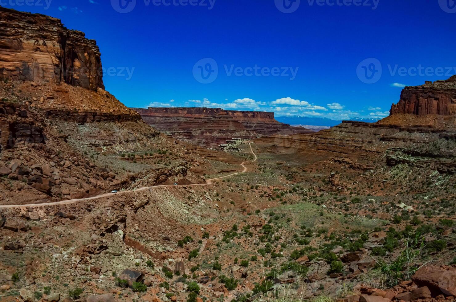 Dirt road at the bottom of the canyon among the layered geological formations of red rocks. photo
