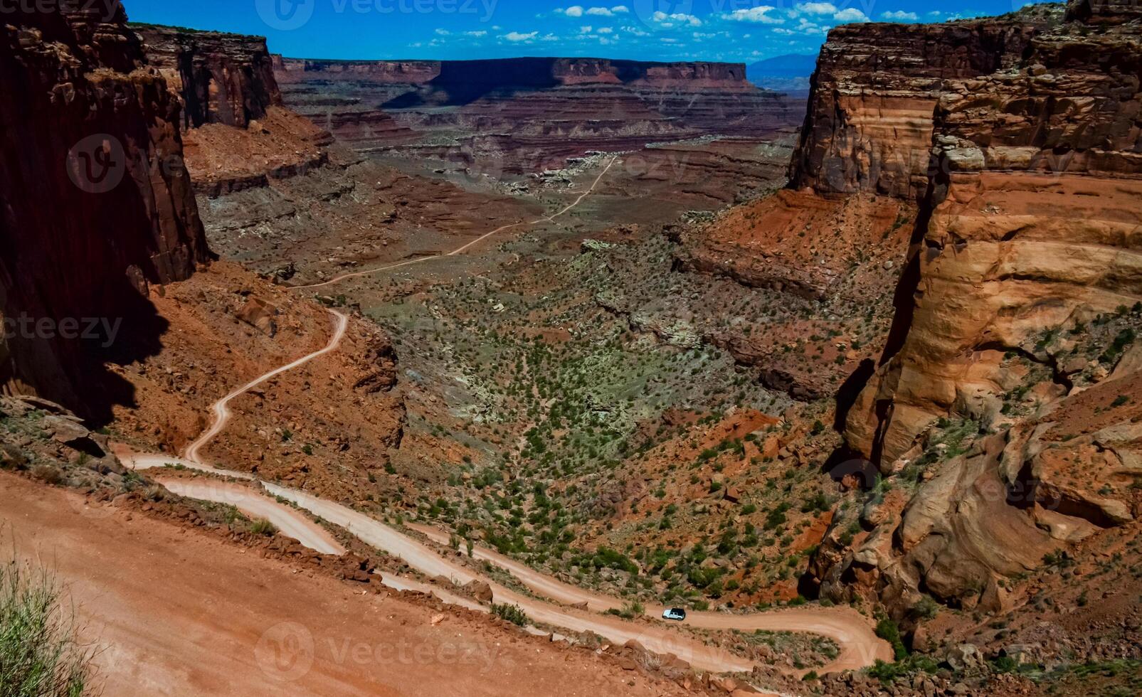 Dirt road at the bottom of the canyon among the layered geological formations of red rocks. photo
