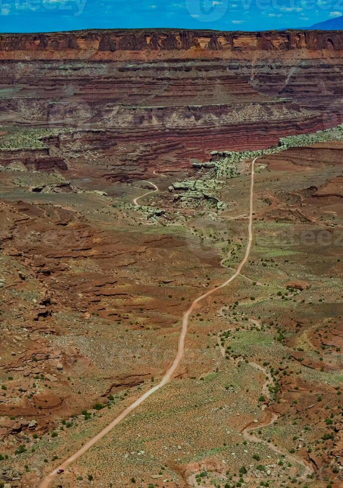 Dirt road at the bottom of the canyon among the layered geological formations of red rocks. photo