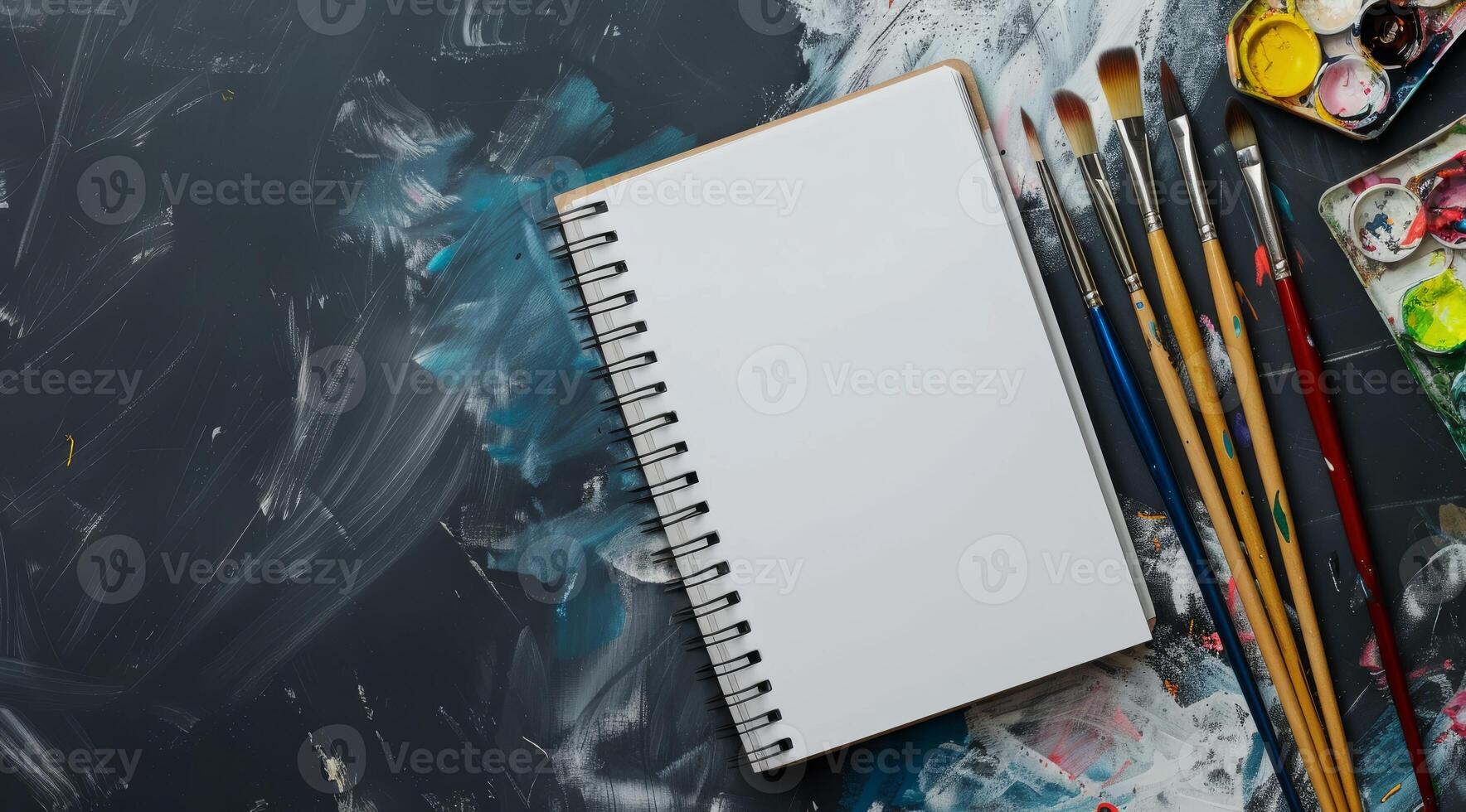 A pristine, blank sketchbook is elegantly surrounded by an array of colorful paint brushes and a lively, vibrant palette, creating an ideal environment for endless artistic inspiration and creativity photo
