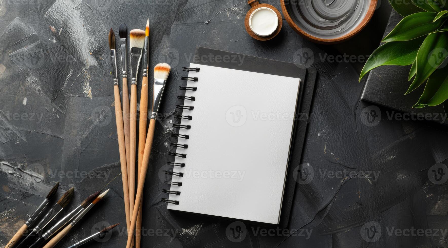 This stylish mockup features a blank notebook, colorful paint brushes, and a vibrant green plant, ideal for showcasing artistic projects and inspiring creativity through visual representation photo