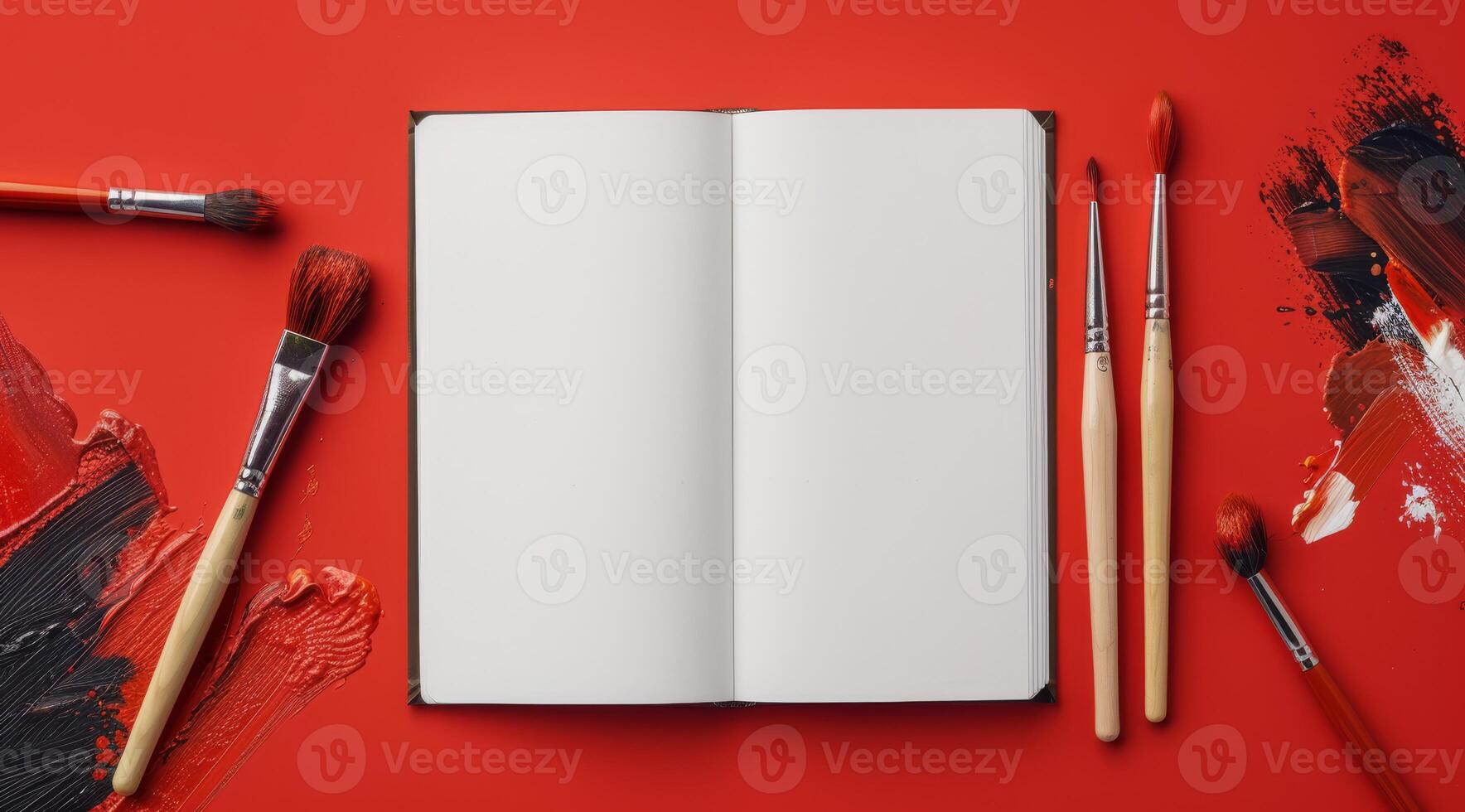 A blank notebook elegantly rests on a vivid red background, surrounded by paint brushes and colorful strokes, sparking inspiration and creativity for all artistic endeavors and expression photo