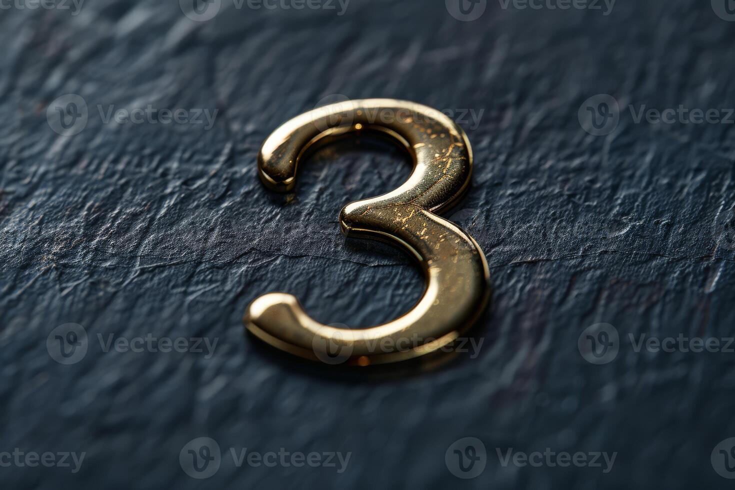 A detailed closeup of a shiny gold number three resting on a dark, textured surface that is ideal for design projects photo