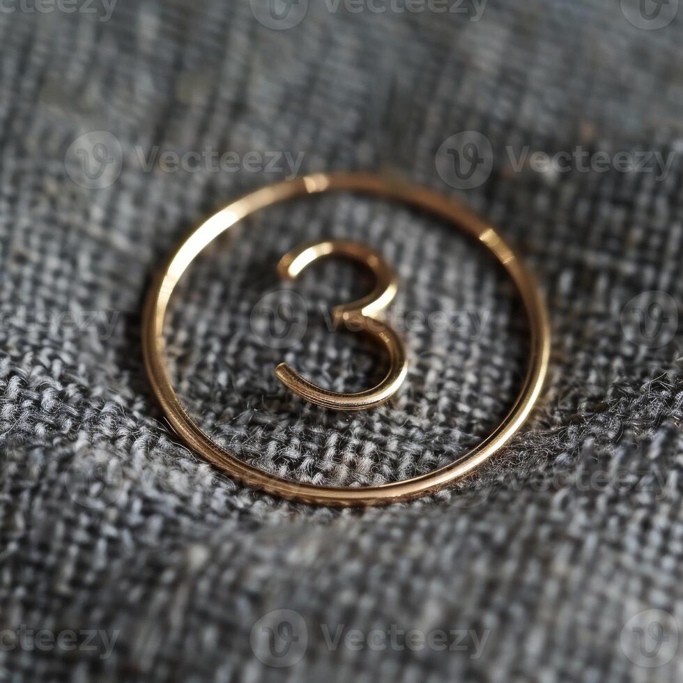 An elegantly sleek gold pendant that prominently features the number 3, beautifully displayed on rich, textured fabric photo