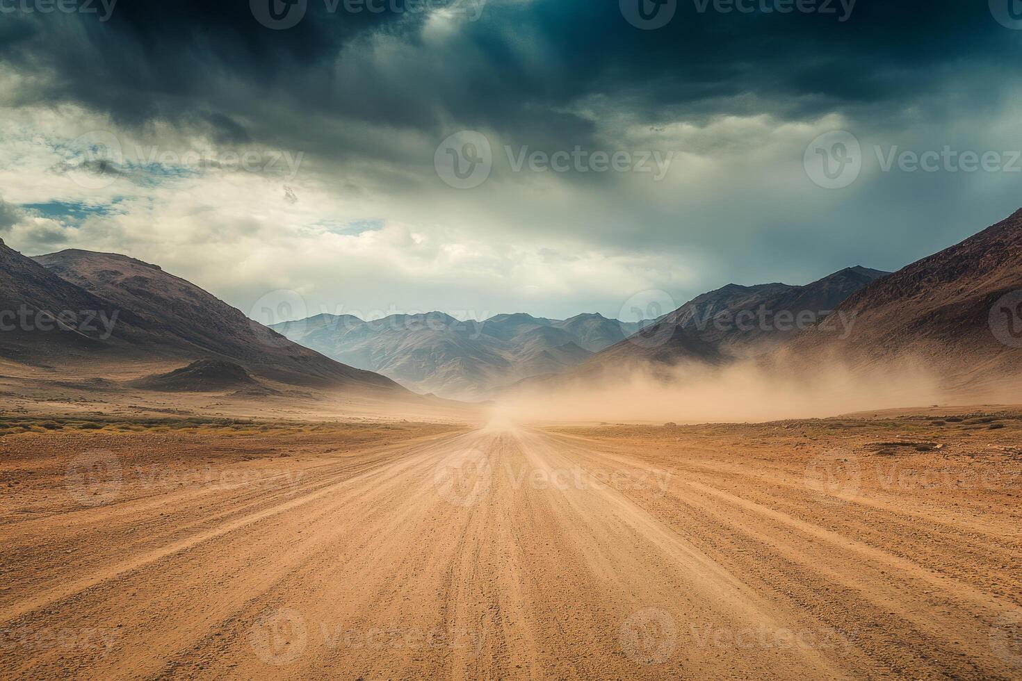 A long gravel road extends towards the distant horizon, bordered by parched, dusty terrain and towering mountains beneath an overcast, moody sky that evokes a sense of adventure and exploration photo