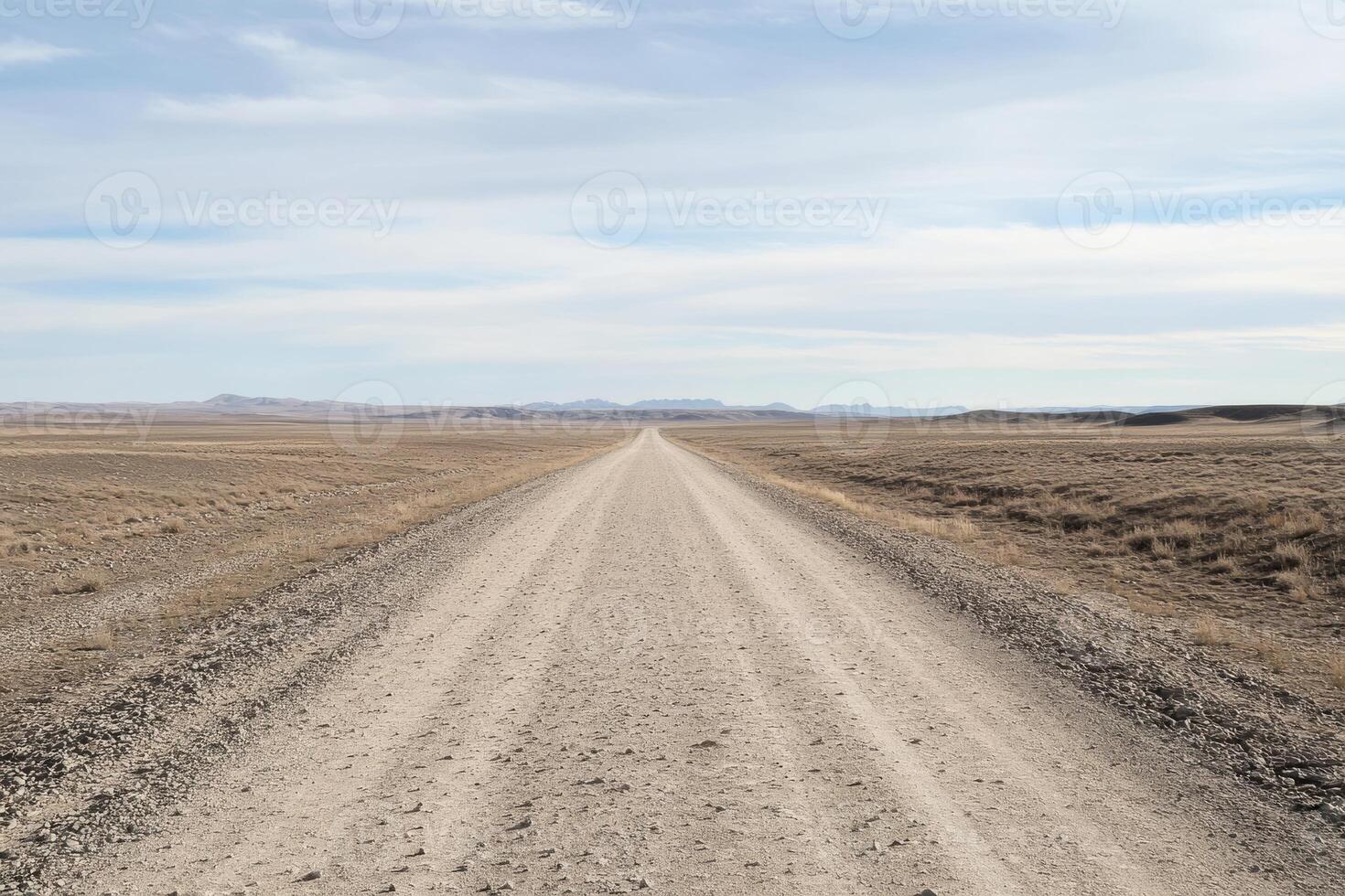A long gravel road stretches into the horizon, winding through a barren landscape under a bright blue sky with fluffy clouds, inviting exploration and adventure in natures wide, open surroundings photo