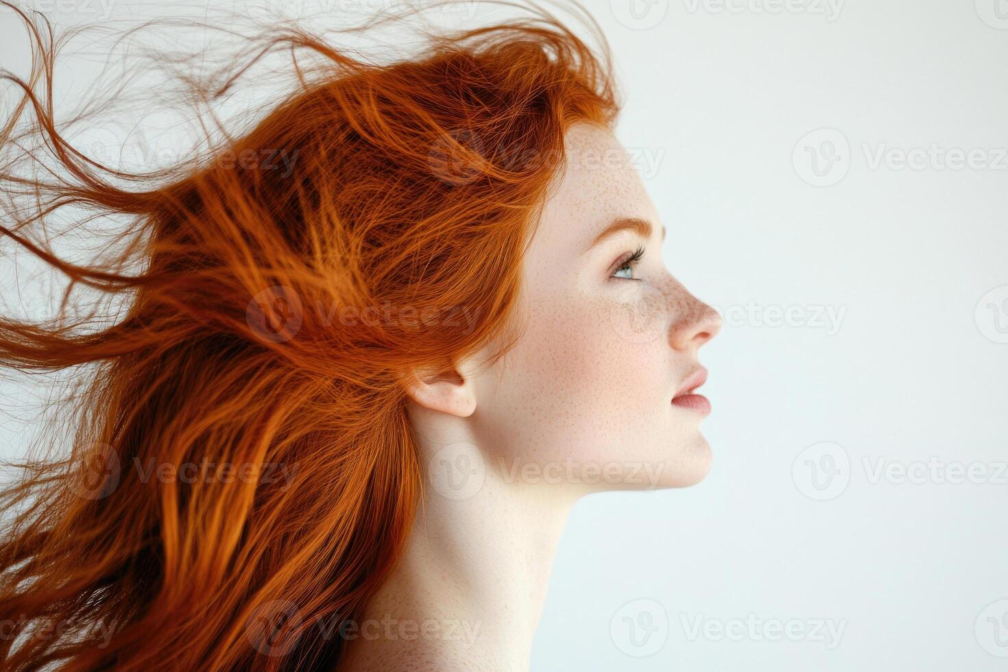 Profile portrait of a beautiful red-haired young woman with flowing hair on a white studio background. photo