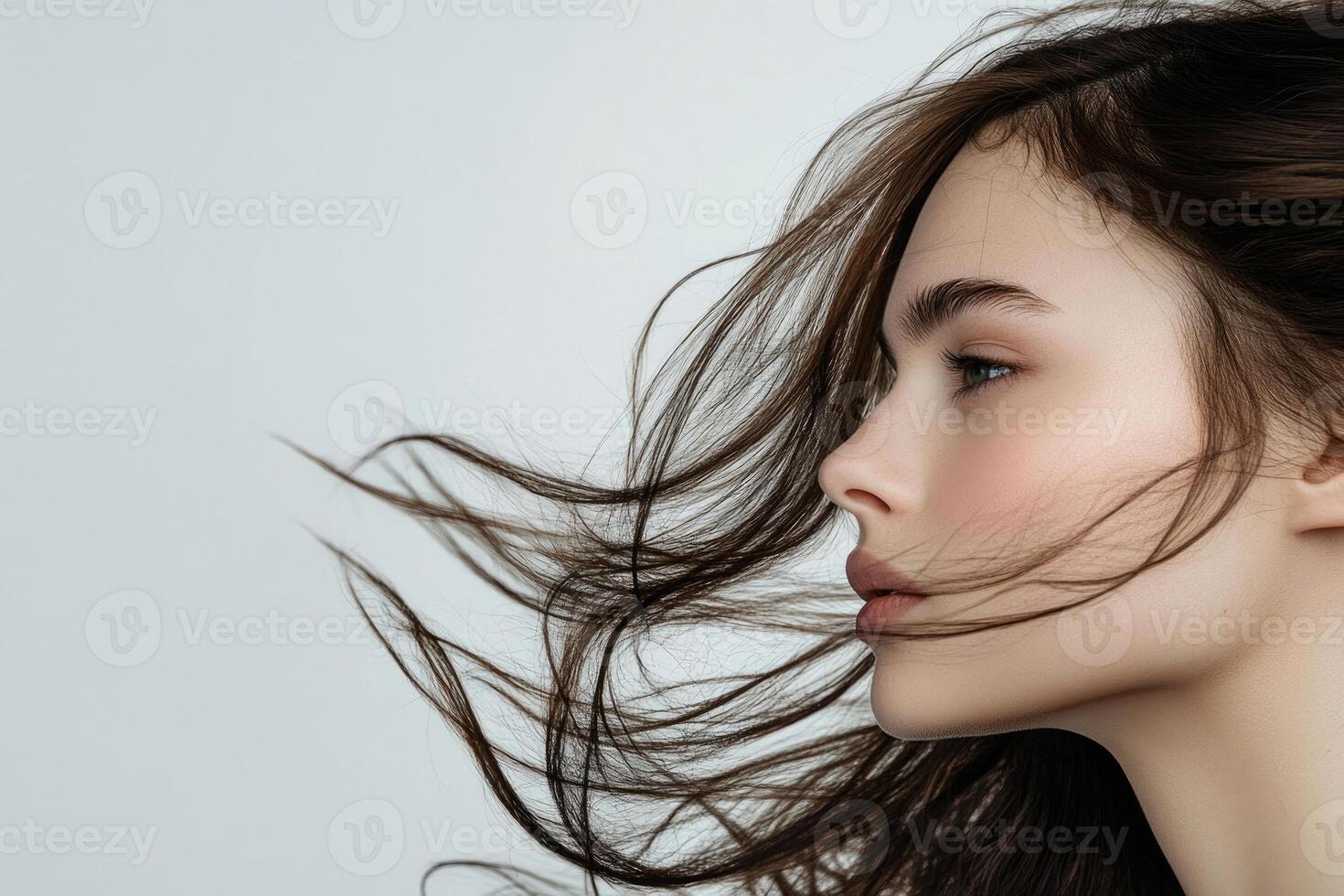 A profile portrait of a young brunette woman with flowing hair on a white background. photo