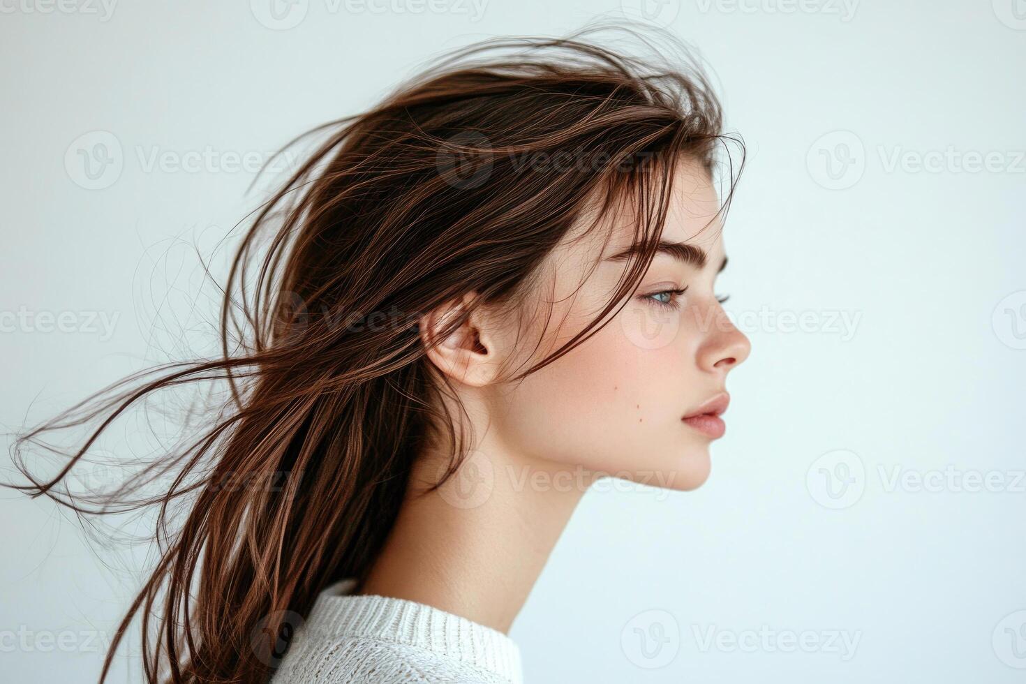 Profile shot of a beautiful young brunette with wind-swept hair against a white backdrop. photo
