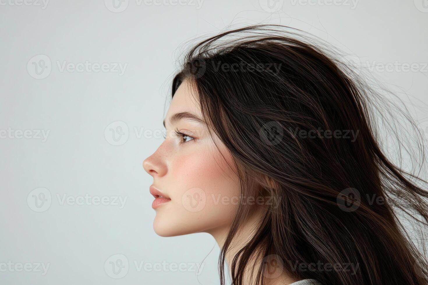 Profile shot of a beautiful young brunette with wind-swept hair against a white backdrop. photo