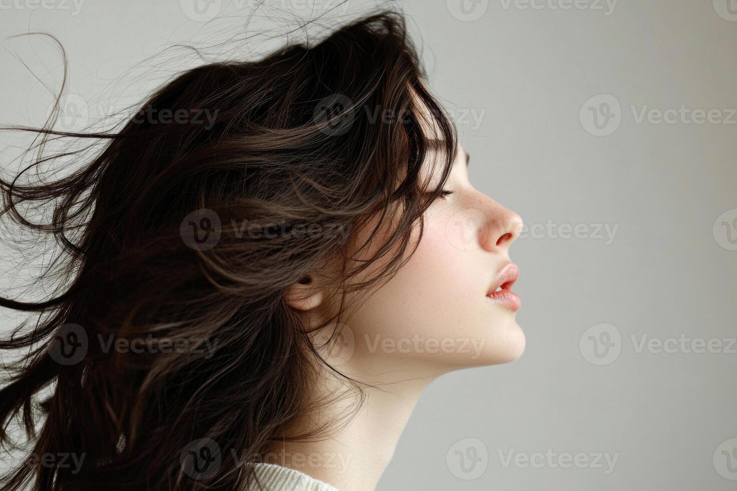 Profile shot of a beautiful young brunette with wind-swept hair against a white backdrop. photo